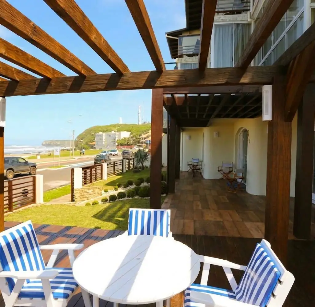 Deck com pergolado e mesa da Pousada Praia do Meio com a orla da Prainha, em Torres, ao fundo